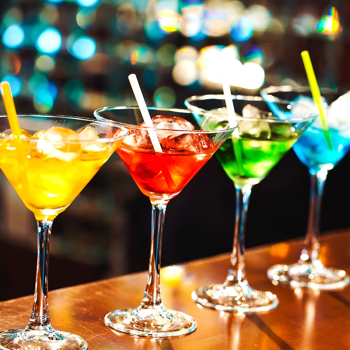 four different colored martinis lined up next to each other on a bar